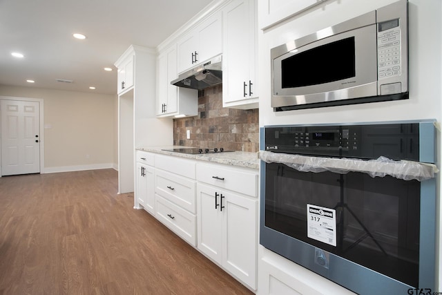 kitchen with wood finished floors, under cabinet range hood, light stone counters, appliances with stainless steel finishes, and backsplash