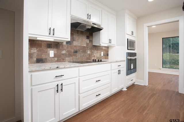 kitchen featuring decorative backsplash, wood finished floors, oven, stainless steel microwave, and under cabinet range hood