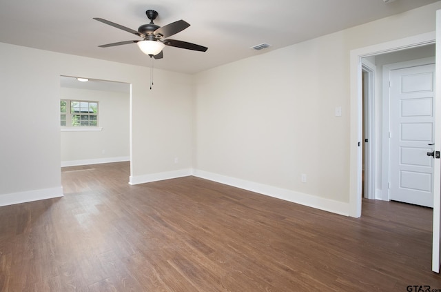 empty room with dark wood-style flooring, a ceiling fan, visible vents, and baseboards