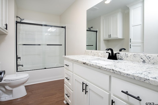 bathroom featuring toilet, enclosed tub / shower combo, wood finished floors, and vanity