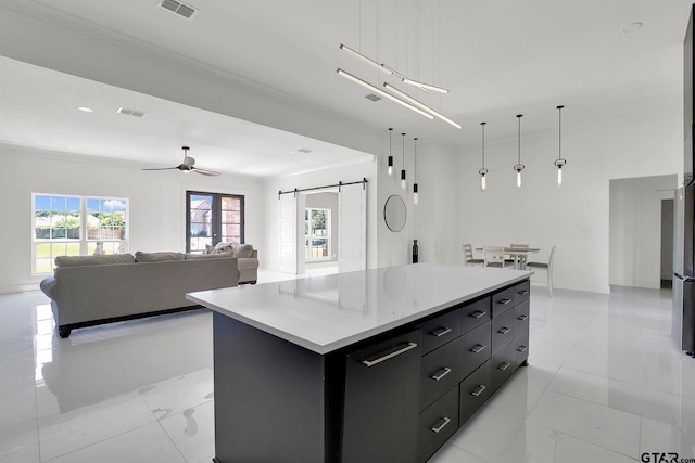 kitchen featuring ceiling fan, hanging light fixtures, a barn door, crown molding, and a kitchen island