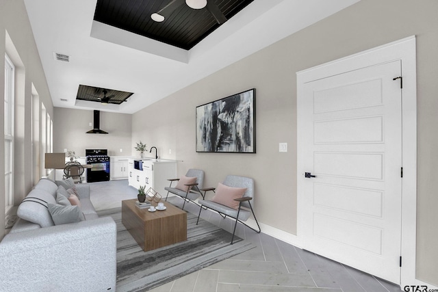 living room with a raised ceiling, light parquet floors, ceiling fan, and sink