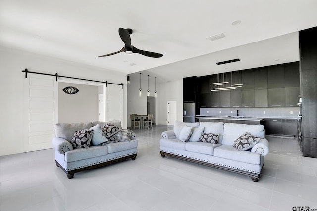 tiled living room featuring a barn door, ceiling fan, and sink