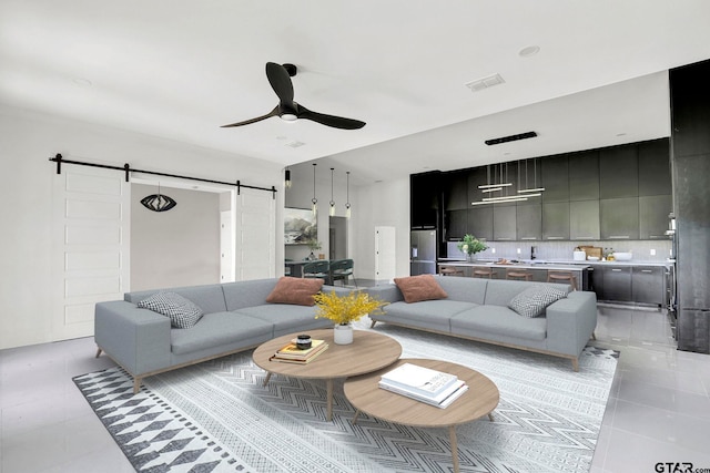 tiled living room with ceiling fan, a barn door, and sink