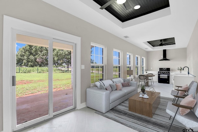 living room with a tray ceiling, ceiling fan, and sink