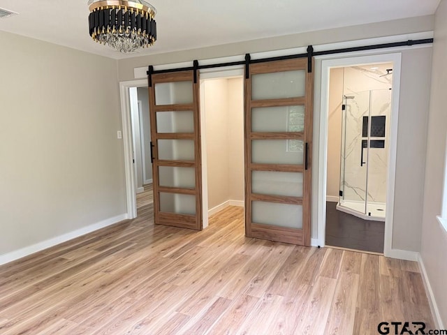 1113 Swanson Dr, Palestine, TX 75801 - unfurnished bedroom featuring a barn door, light wood-style floors, baseboards, and a chandelier