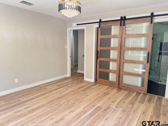 1113 Swanson Dr, Palestine, TX 75801 - empty room featuring a barn door, light wood-type flooring, baseboards, and a chandelier