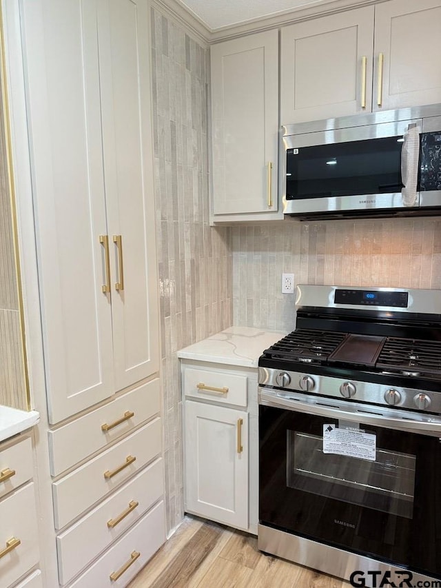 1113 Swanson Dr, Palestine, TX 75801 - kitchen featuring stainless steel appliances, decorative backsplash, light stone counters, light wood-style floors, and white cabinets