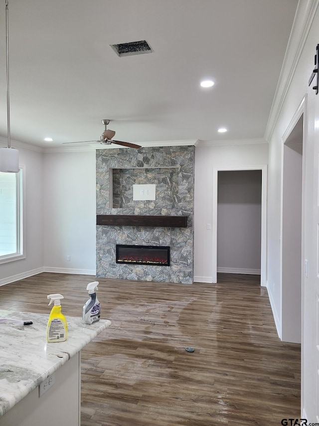 unfurnished living room featuring a stone fireplace, a barn door, dark hardwood / wood-style floors, and crown molding