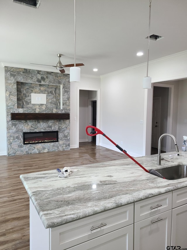 kitchen with wood-type flooring, a stone fireplace, white cabinetry, pendant lighting, and sink