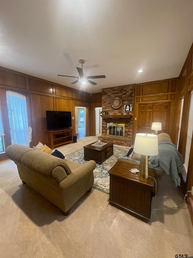 living room featuring light carpet, a brick fireplace, wooden walls, and ceiling fan