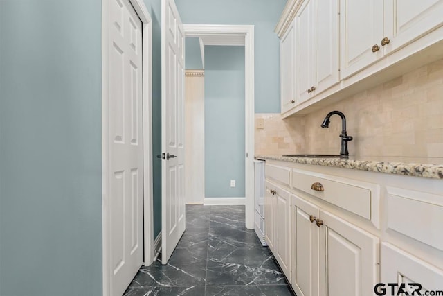 interior space with sink, light stone counters, white cabinets, and backsplash