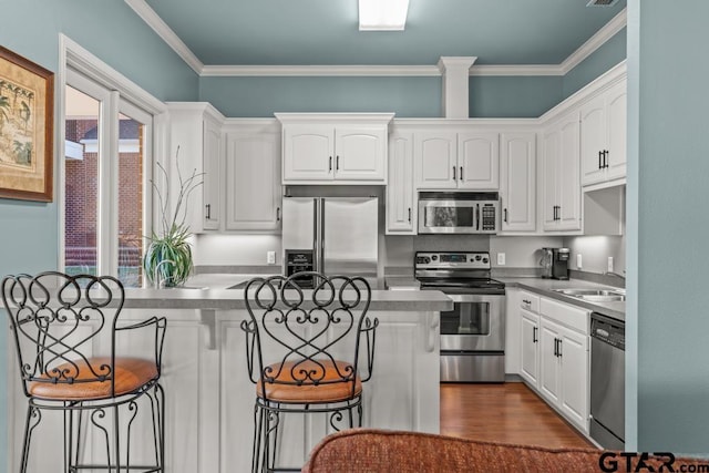 kitchen with a kitchen breakfast bar, stainless steel appliances, crown molding, sink, and white cabinetry