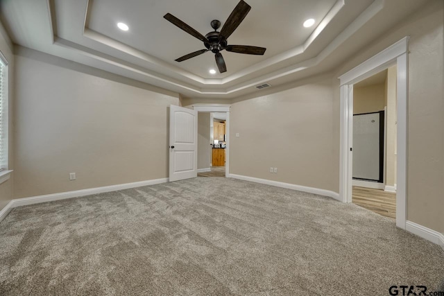 unfurnished bedroom with light carpet, a tray ceiling, and ceiling fan