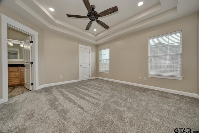 unfurnished bedroom featuring ceiling fan, light carpet, connected bathroom, and a tray ceiling