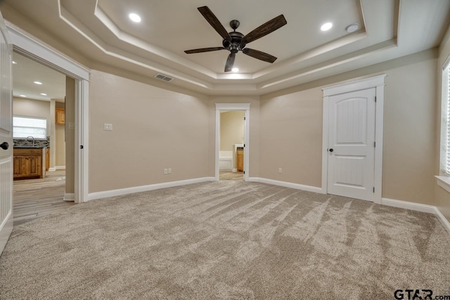 unfurnished bedroom featuring light carpet, a raised ceiling, ceiling fan, and sink