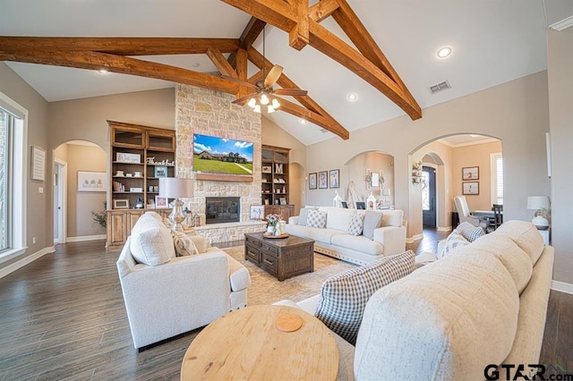 living room featuring beam ceiling, visible vents, a stone fireplace, wood finished floors, and baseboards