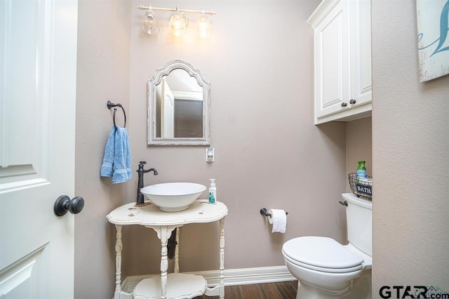 bathroom featuring toilet, a sink, baseboards, and wood finished floors