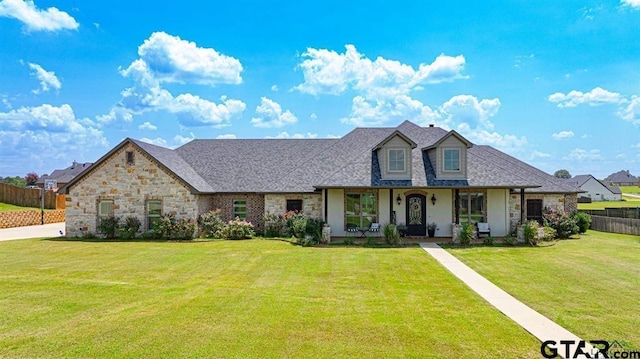 view of front of home with roof with shingles, a porch, fence, stone siding, and a front lawn