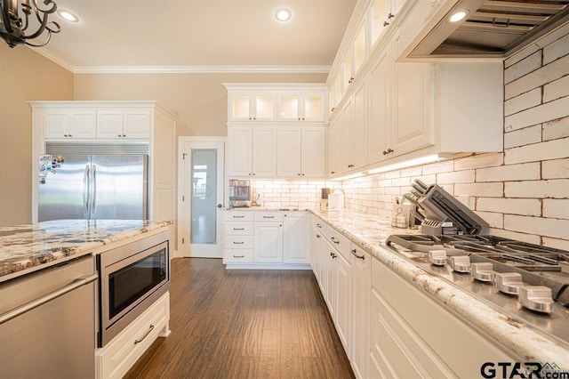 kitchen featuring crown molding, tasteful backsplash, light stone countertops, built in appliances, and extractor fan