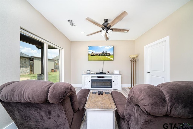 living room featuring baseboards, a fireplace, visible vents, and a ceiling fan