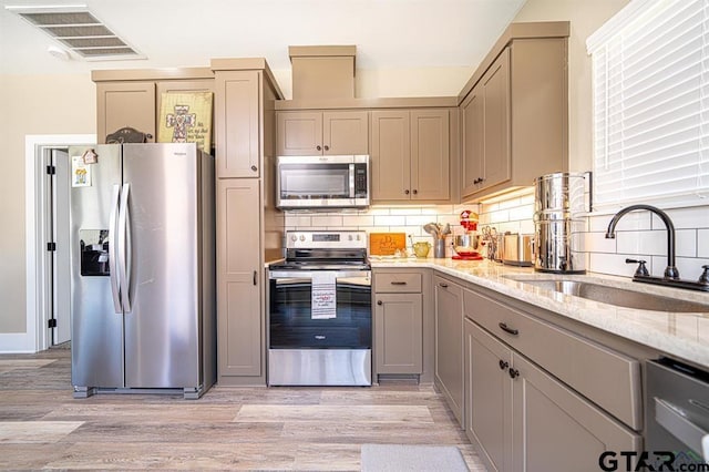 kitchen with visible vents, appliances with stainless steel finishes, light stone countertops, gray cabinetry, and a sink