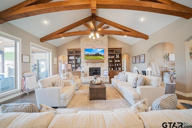 living area with arched walkways, a stone fireplace, and wood finished floors