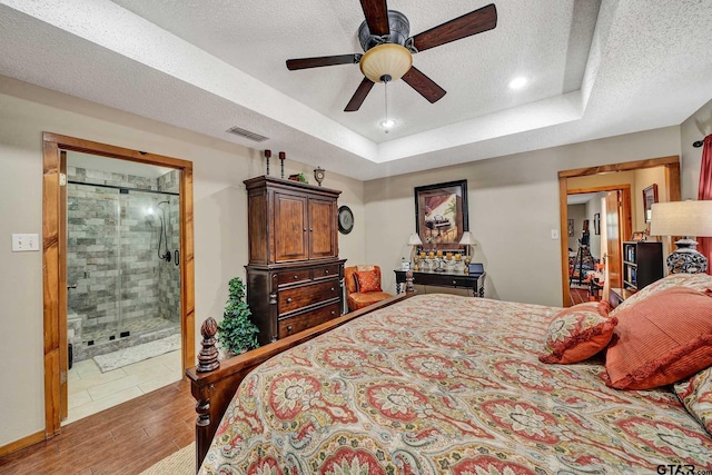 bedroom featuring a textured ceiling, ceiling fan, wood finished floors, visible vents, and a raised ceiling