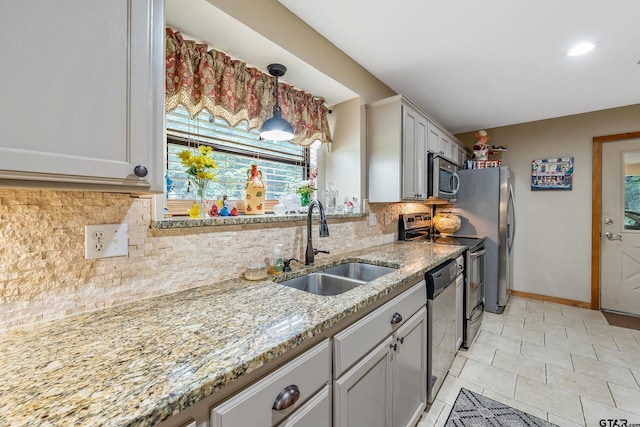 kitchen featuring baseboards, light stone counters, appliances with stainless steel finishes, a sink, and backsplash