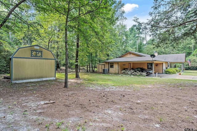 view of yard with a forest view, central AC unit, and an outdoor structure