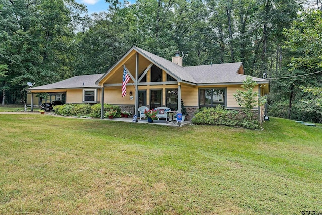 view of front facade featuring stone siding, a chimney, a front lawn, and a carport