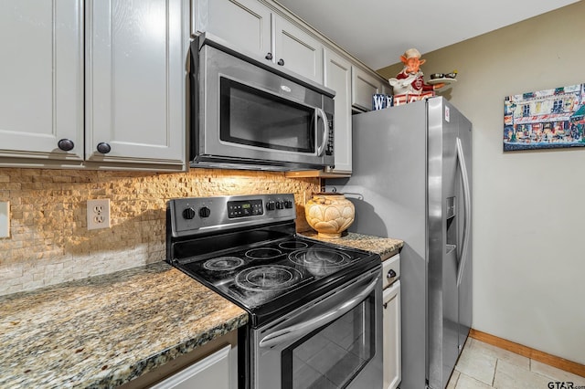 kitchen featuring light tile patterned flooring, stainless steel appliances, baseboards, backsplash, and dark stone counters