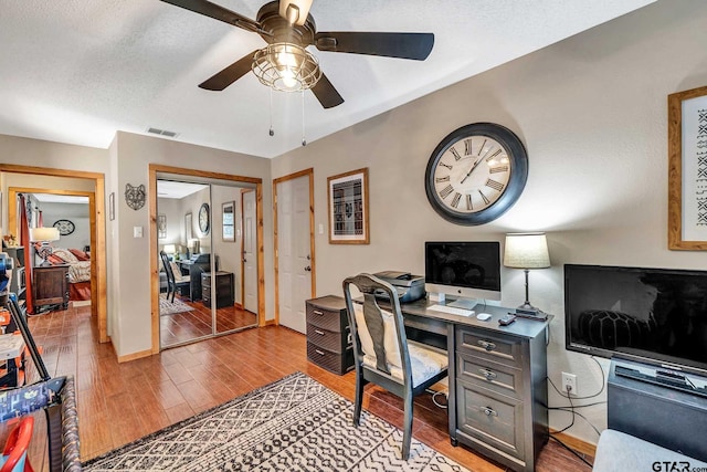 office area featuring a textured ceiling, ceiling fan, visible vents, baseboards, and light wood-type flooring