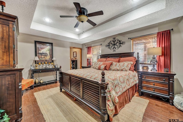 bedroom featuring a raised ceiling, multiple windows, light wood-style flooring, and a textured ceiling