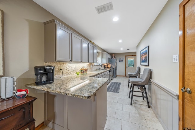 kitchen featuring visible vents, a wainscoted wall, a peninsula, light stone countertops, and a sink