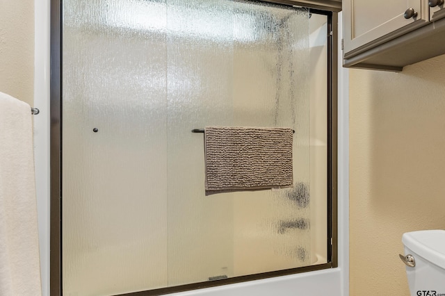 bathroom with toilet and bath / shower combo with glass door