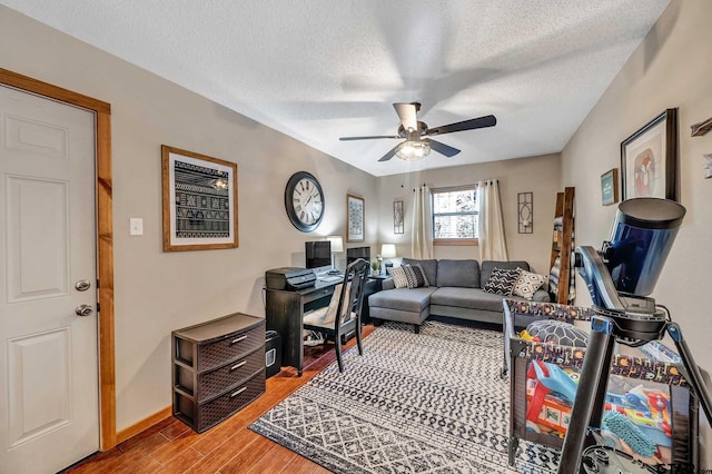 home office featuring a textured ceiling, baseboards, a ceiling fan, and light wood-style floors