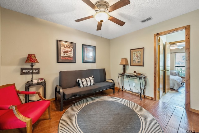 living area with visible vents, ceiling fan, a textured ceiling, wood finished floors, and baseboards