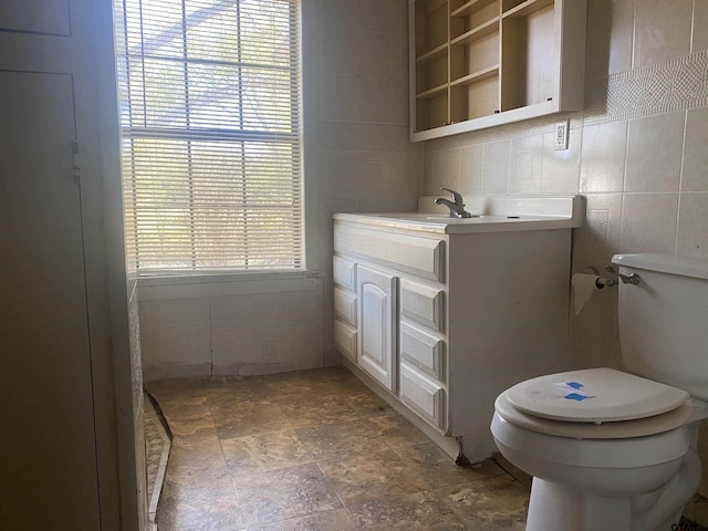 bathroom with vanity, toilet, plenty of natural light, and tile walls