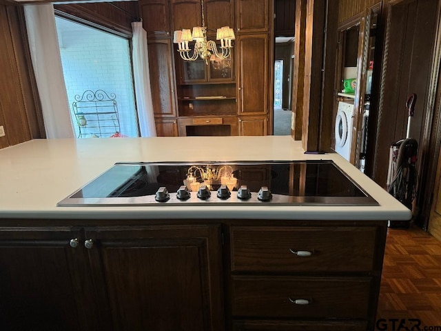 kitchen with black electric stovetop, dark parquet flooring, washer / dryer, and an inviting chandelier