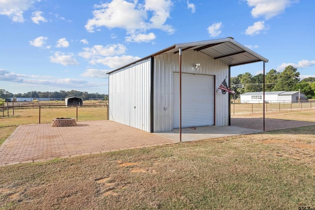 view of outdoor structure with a garage, a yard, a rural view, and a fire pit