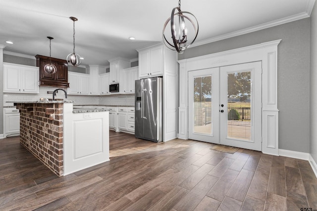 kitchen featuring dark wood-type flooring, black microwave, an island with sink, pendant lighting, and stainless steel fridge