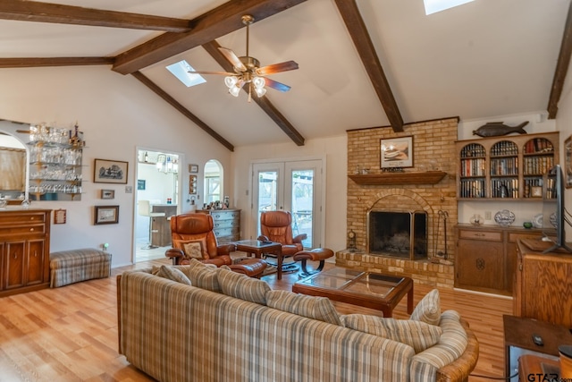 living room with a brick fireplace, a skylight, light hardwood / wood-style floors, and ceiling fan