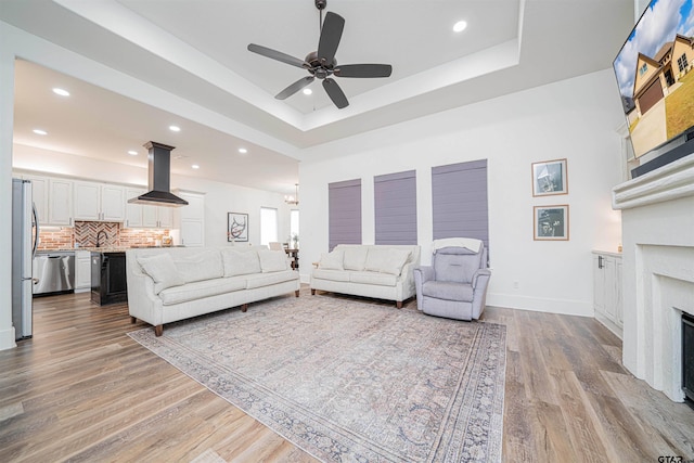 living room featuring a fireplace, a raised ceiling, sink, ceiling fan, and light hardwood / wood-style flooring