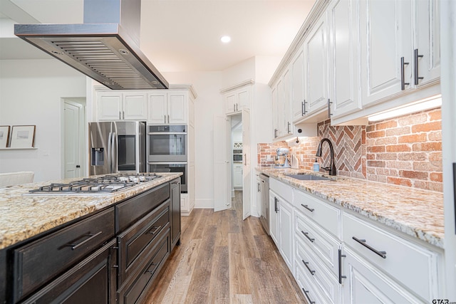 kitchen with exhaust hood, light stone countertops, white cabinetry, light wood-type flooring, and appliances with stainless steel finishes