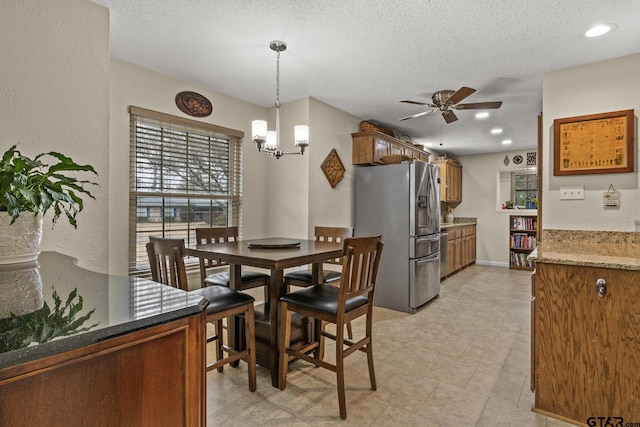 dining area featuring ceiling fan with notable chandelier and a textured ceiling