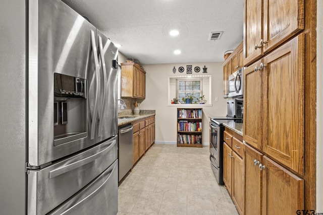 kitchen with appliances with stainless steel finishes, sink, light tile patterned floors, light stone countertops, and a textured ceiling