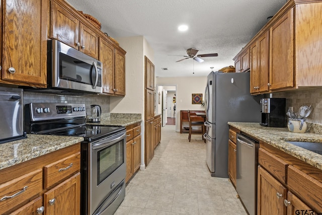 kitchen with light stone counters, a textured ceiling, appliances with stainless steel finishes, ceiling fan, and backsplash