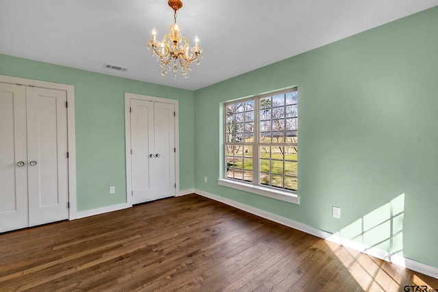 unfurnished bedroom with dark wood-type flooring, two closets, and a notable chandelier