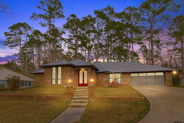 prairie-style home featuring an attached garage, brick siding, driveway, and a front lawn